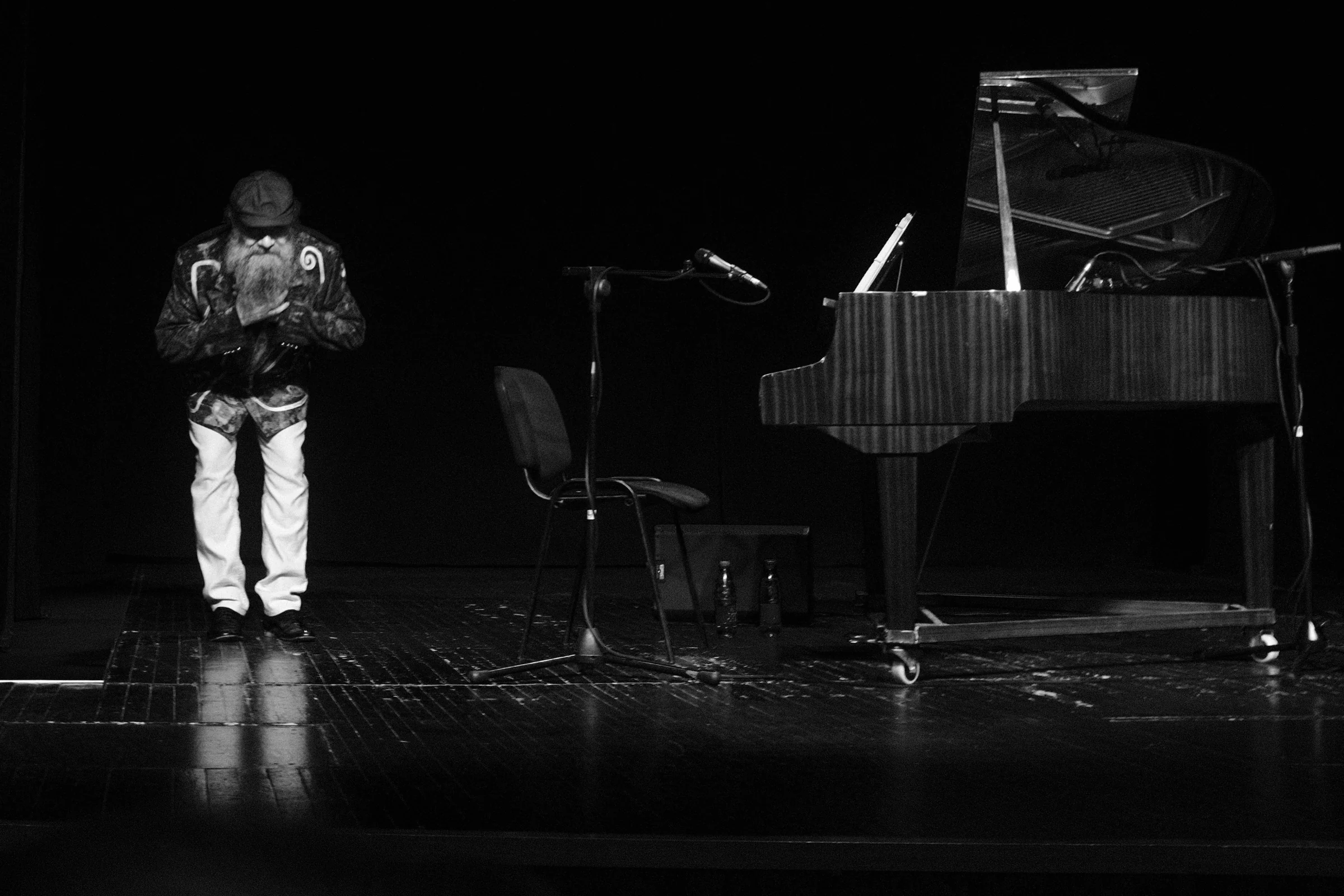 A performer bowing beside a grand piano on a dark stage
